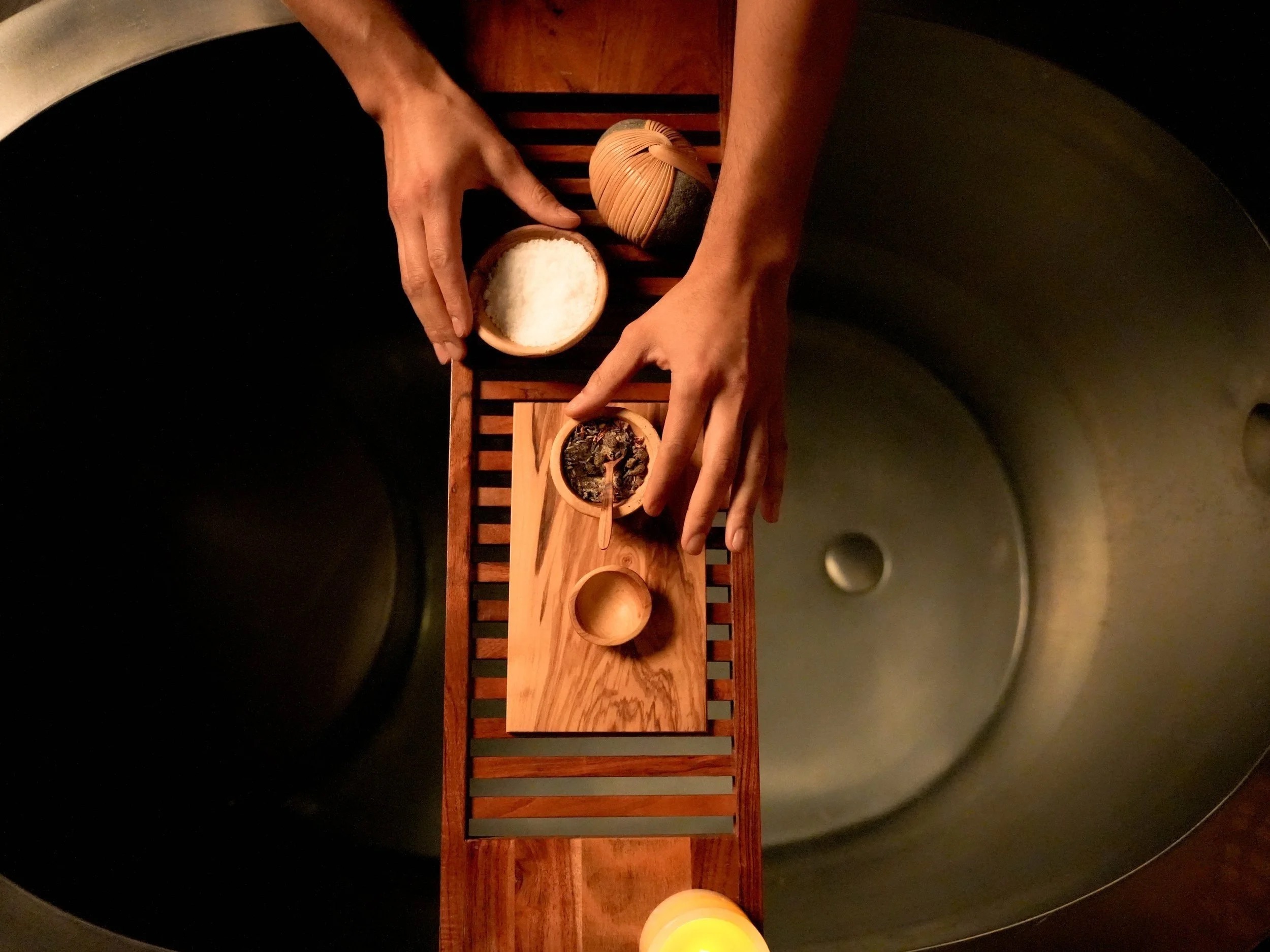 Hands preparing bath herbs and salt over a private soaking tub